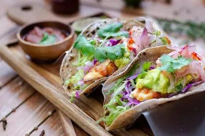 two tacos on a wooden tray with a bowl of dips at The Stones Hotel - Legian Bali in Kuta