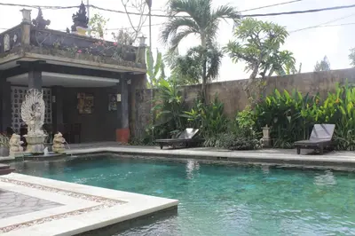 a swimming pool in a yard with chairs and a building at Mangga Bali Inn in Legian