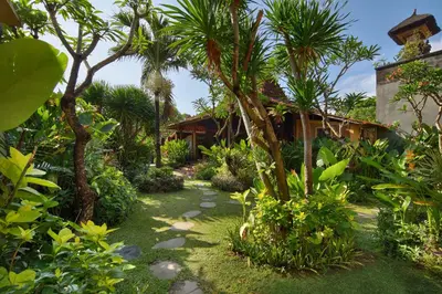 a garden with palm trees and a house at Mahe Garden Kuta Villas by Kamara in Kuta