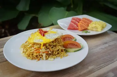 two plates of food on a table with noodles and fruit at Kubu Kak Dudung Villas in Jimbaran