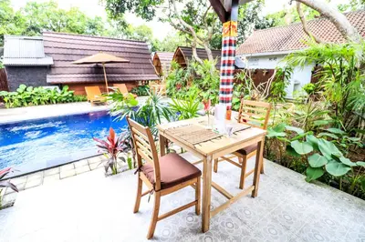 a wooden table and chairs next to a swimming pool at Kubu Kak Dudung Villas in Jimbaran