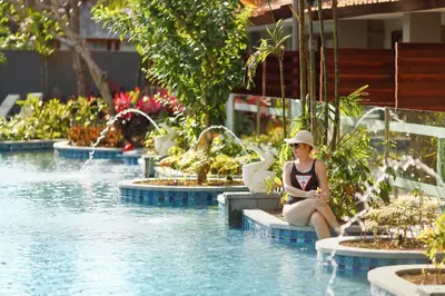 a woman in a hat sitting next to a swimming pool at Bali Dynasty Resort in Kuta