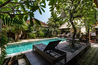 a pool at a villa with chairs and trees at Eddys Cottages & Villa in Legian