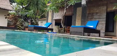 two chairs and a swimming pool in front of a building at Eddys Cottages & Villa in Legian