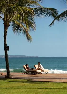 two people sitting in lounge chairs on the beach at The Samaya Seminyak Bali in Seminyak