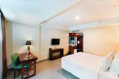 a bedroom with a bed and a desk and a television at Swiss-Belhotel Rainforest in Kuta