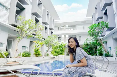 a woman sitting on a chair next to a swimming pool at The Rooms Apartment Bali by ARM Hospitality in Denpasar