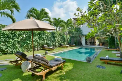 a pool with chairs and an umbrella next to a yard at Villa Chocolat Seminyak in Seminyak