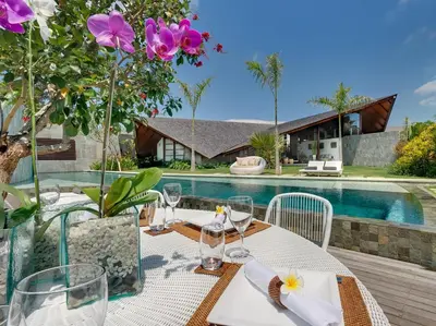 a table with wine glasses and flowers on a table in front of a pool at The Layar - Designer Villas and Spa in Seminyak