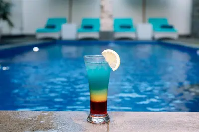 a drink with a lime slice in front of a pool at Kubu Benoa Guest House in Nusa Dua