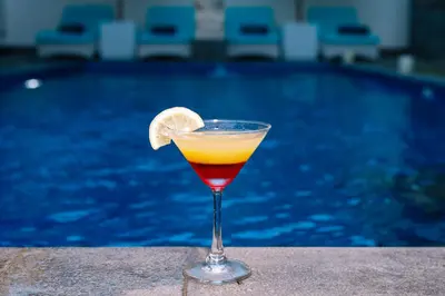 a drink in a glass next to a swimming pool at Kubu Benoa Guest House in Nusa Dua