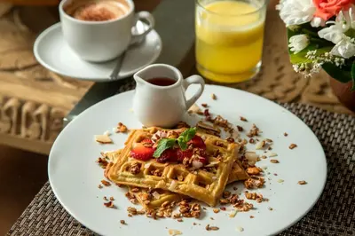 a plate of waffles with strawberries and a cup of coffee at The Luxury Collection, Monaco Blu in Seminyak