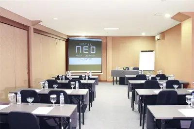 a conference room with tables and chairs and a screen at Hotel Neo - Kuta, Jelantik in Legian