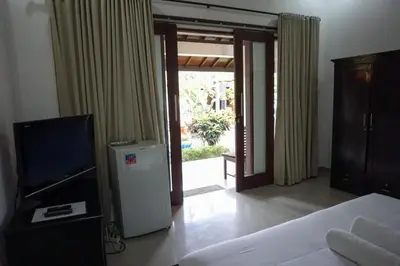 a bedroom with a bed and a television and a door at Ary Guest House in Canggu