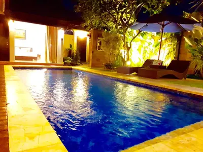 a swimming pool at night with an umbrella at Villa Davenny in Seminyak