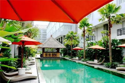 a swimming pool with chairs and umbrellas in a hotel at b Hotel Bali & Spa in Denpasar