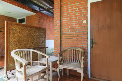 two chairs and a table on a porch with a brick wall at Ayu Lili Garden Hotel Kuta in Kuta