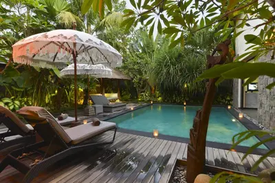 a swimming pool with chairs and an umbrella at Elok Villas in Seminyak