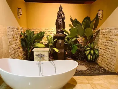 a bath tub in a bathroom with a statue at Three Brothers Bali Legian Bungalows & Villas in Legian