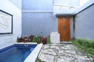 a house with a swimming pool and a wooden door at Hoki Villa by Urbanview Villa in Kerobokan