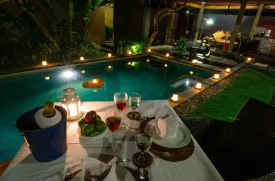 a table with wine glasses and food next to a swimming pool at Imani Villas in Canggu