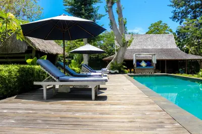 a deck with chairs and an umbrella next to a swimming pool at Chanteak Bali in Jimbaran