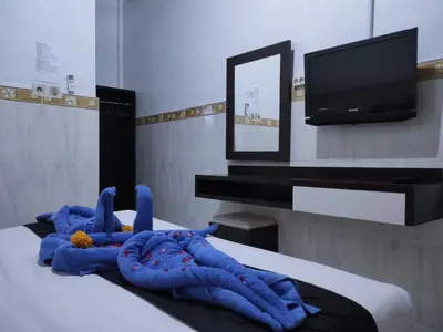a room with a bed with blue blankets and a tv at Pondok DenAyu Homestay in Kuta