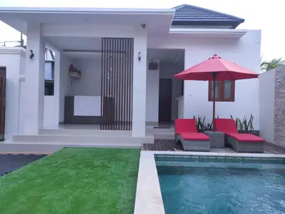 a house with a pool and two chairs and an umbrella at Pondok DenAyu Homestay in Kuta