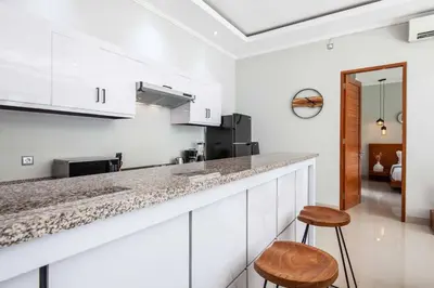 a kitchen with white cabinets and a counter and two stools at Villa Voyage 4 in Seminyak