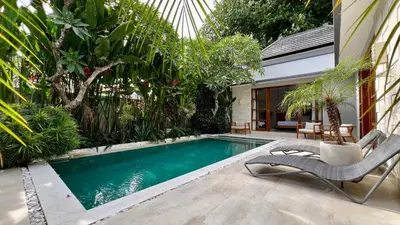 a swimming pool in a garden with a chair next to it at Villa Voyage 5 in Seminyak
