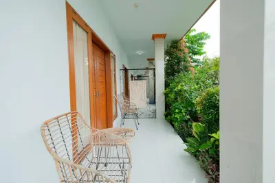 a balcony with two chairs and a wooden door at Kadek Bagus Guesthouse Denpasar Mitra RedDoorz in Kerobokan