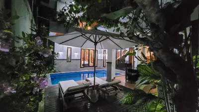 a patio with an umbrella and chairs and a pool at Ramantika Sunset Bay in Nusa Dua