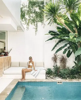 a woman sitting on a couch next to a swimming pool at THE HIDDEN TREE CANGGU 100 meter to beach in Canggu