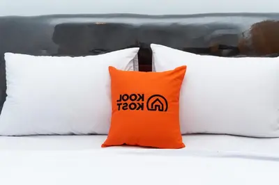 an orange pillow sitting on a bed with three white pillows at KoolKost at Poppies Lane Street - Minimum stay 30 nights in Denpasar