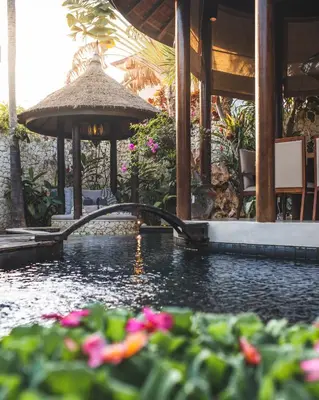 a swimming pool with a umbrella and some flowers at Sandi Kala Villas in Kerobokan
