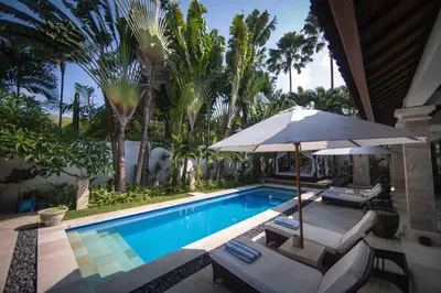 a swimming pool with two chairs and an umbrella at Villa Alu Lima in Seminyak