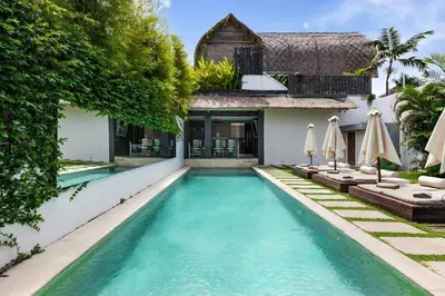 a swimming pool in front of a house with umbrellas at Saga Villas ULTRA in Seminyak