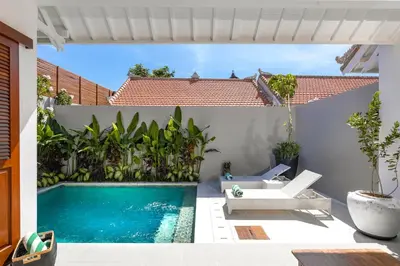 a swimming pool in a backyard with a white wall at Villa Revo in Seminyak