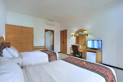 a hotel room with two beds and a desk at Puri Naga Beachfront Cottages in Legian