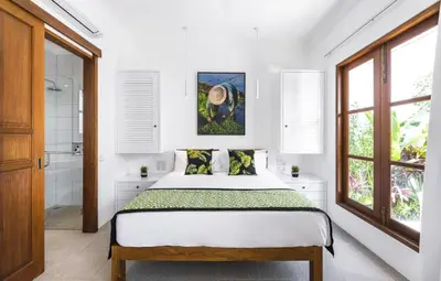 a white bedroom with a bed and two windows at Villa Alfie in Seminyak