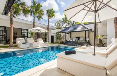 a pool with chairs and an umbrella next to a house at Villa Lora in Seminyak
