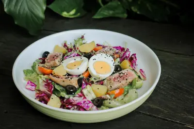 a salad with eggs in a white bowl on a table at Grandmas Plus Hotel Airport in Kuta