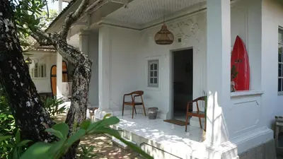 a white house with two chairs on the porch at Endless Summer Surf Camp Kuta in Kuta