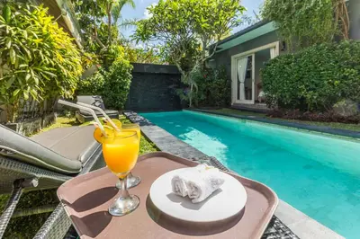 a glass of orange juice on a table next to a swimming pool at VILLA Nuri Merah 2 in Seminyak
