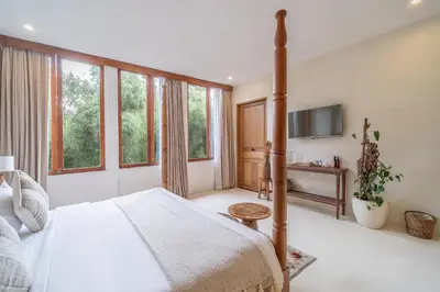 a bedroom with a bed and a tv and windows at White Goose Boutique Hotel in Canggu