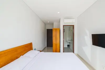 a bedroom with a white bed and a bathroom at Dharma Guest House Seminyak RedPartner in Seminyak