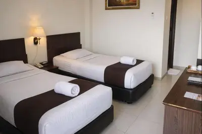 a hotel room with two beds and a desk at Manggar Indonesia Hotel in Kuta