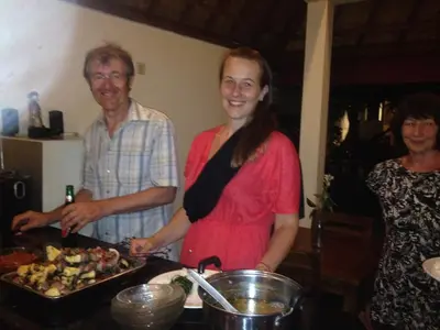 three people standing in a kitchen with a tray of food at Puri Clinton Bali in Nusa Dua
