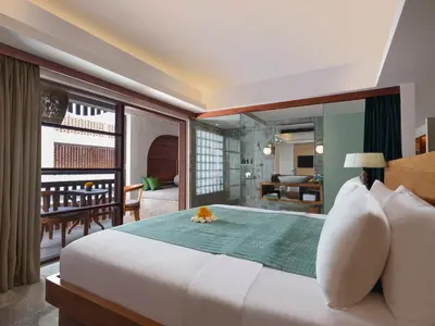 a bedroom with a large white bed and a living room at Amnaya Resort Nusa Dua in Nusa Dua