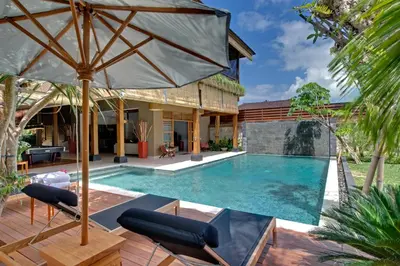 an outdoor pool with chairs and an umbrella at Villa Kinaree Estate in Seminyak